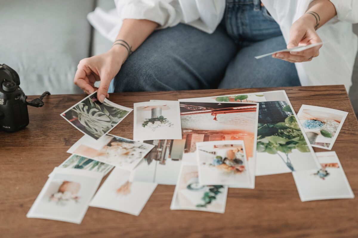 Ruky vyberajú vytlačené fotografie na drevenom stole pri fotoaparáte.