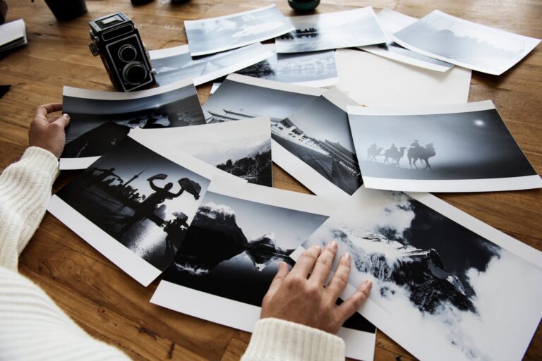 Čiernobiele papierové fotografie rozložené na drevenom stole pri fotoaparáte.