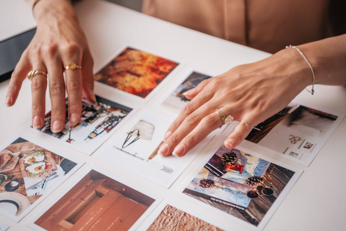 Ruky rozkladajú viaceré vytlačené fotografie a papierové návrhy na stole.